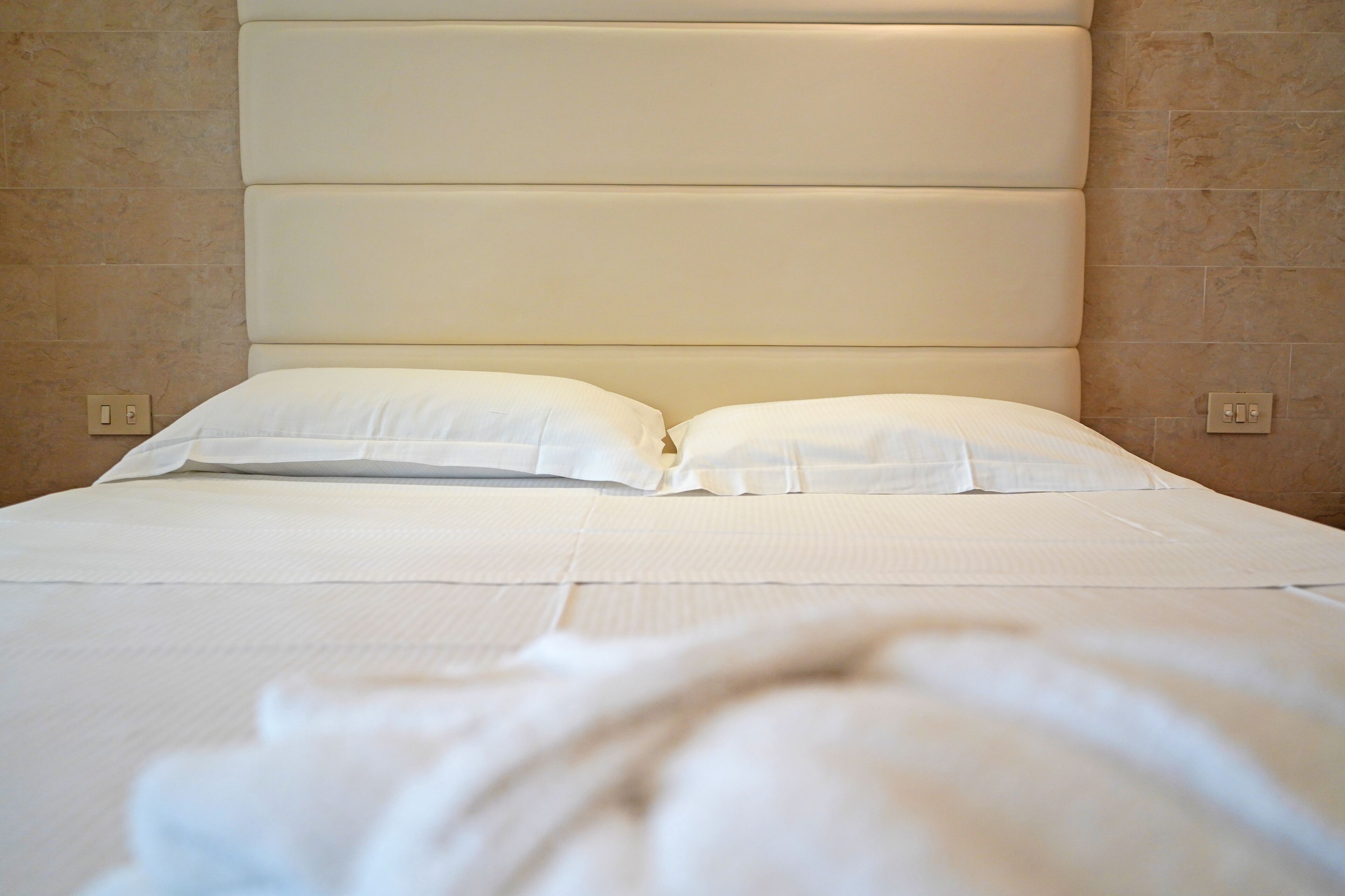 A neatly made bed with a padded headboard and two pillows.