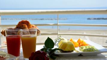 Un plateau de petit-déjeuner avec des croissants, des fruits et des verres de jus, posé sur une table offrant une vue sur la mer.