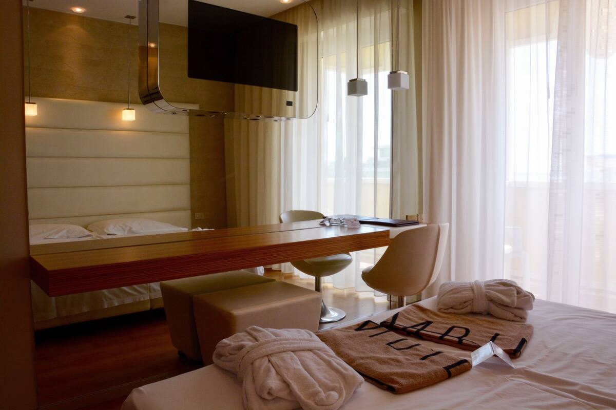 A hotel room with a bed, a desk, a chair, a TV, and a window with curtains.