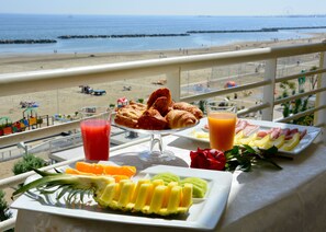 A table with breakfast items including croissants, fruit, and juice, overlooking a beach with umbrellas and people. - Ambienthotels Panoramic (Rimini)