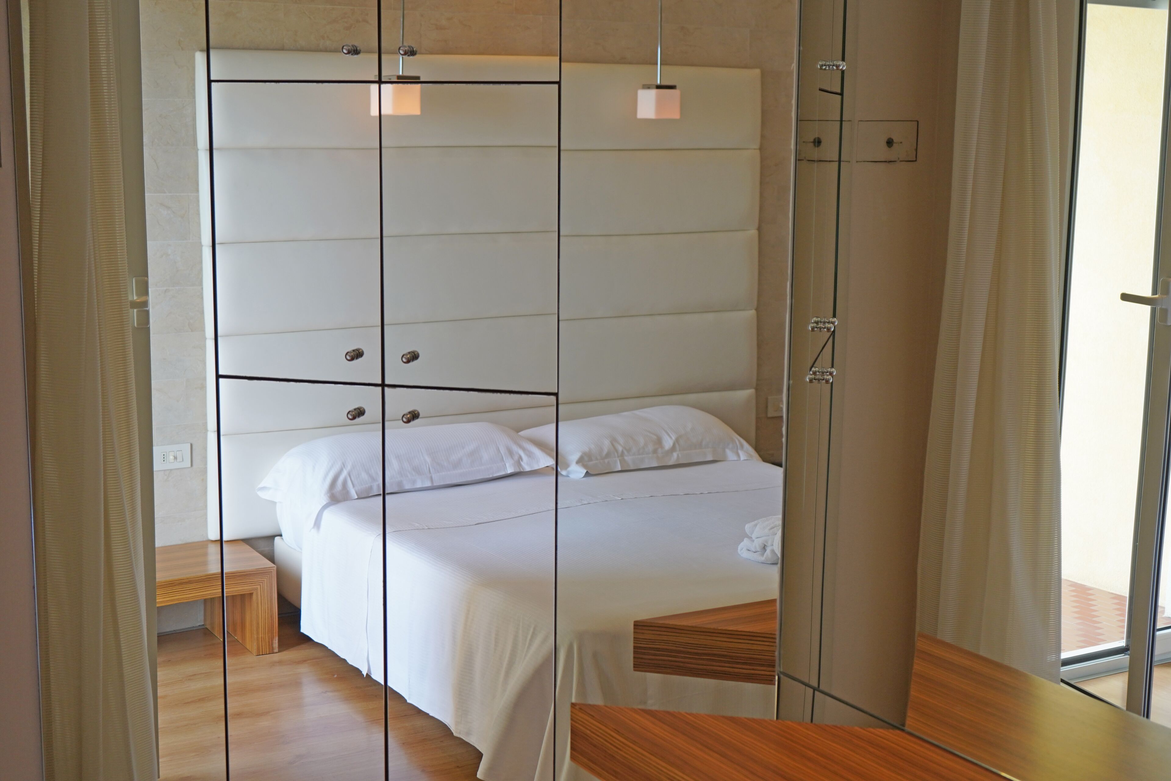 A modern bedroom with a large bed, a wooden bedside table, and a mirror.
