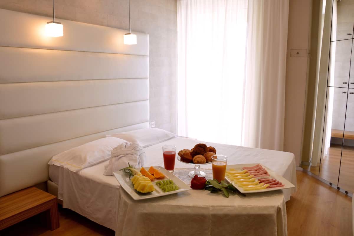 A neatly made bed with a breakfast tray including fruits, pastries, and beverages.