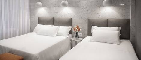 A modern hotel room with two beds, a small round table with a vase of flowers, and a marble-patterned wall.