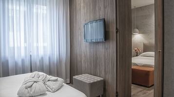 A hotel room with a bed, a TV mounted on the wall, a small ottoman, and a bathroom visible through an open door.