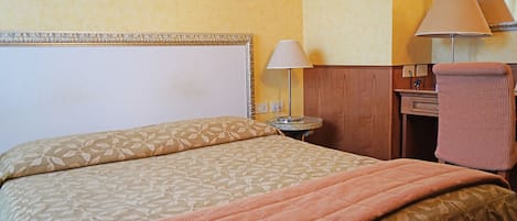 Una habitación de hotel con una cama, un escritorio, una lámpara y una silla.