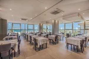 Un'ampia sala da pranzo con tavoli apparecchiati per gli ospiti, grandi finestre con vista sull'oceano e un design d'interni moderno.