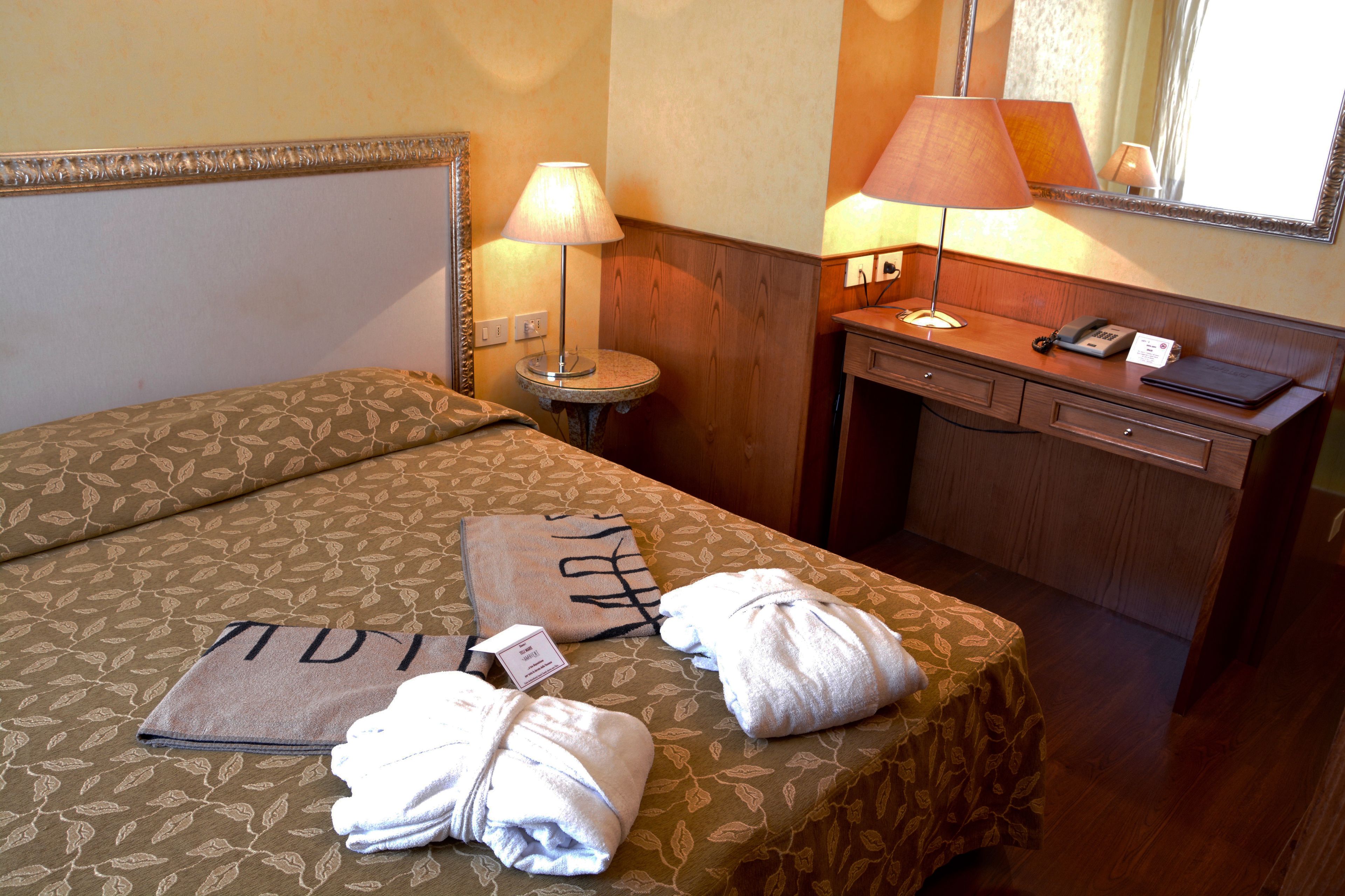Ein Hotelzimmer mit Bett, Nachttisch mit Lampe, Schreibtisch mit Telefon und Spiegel.