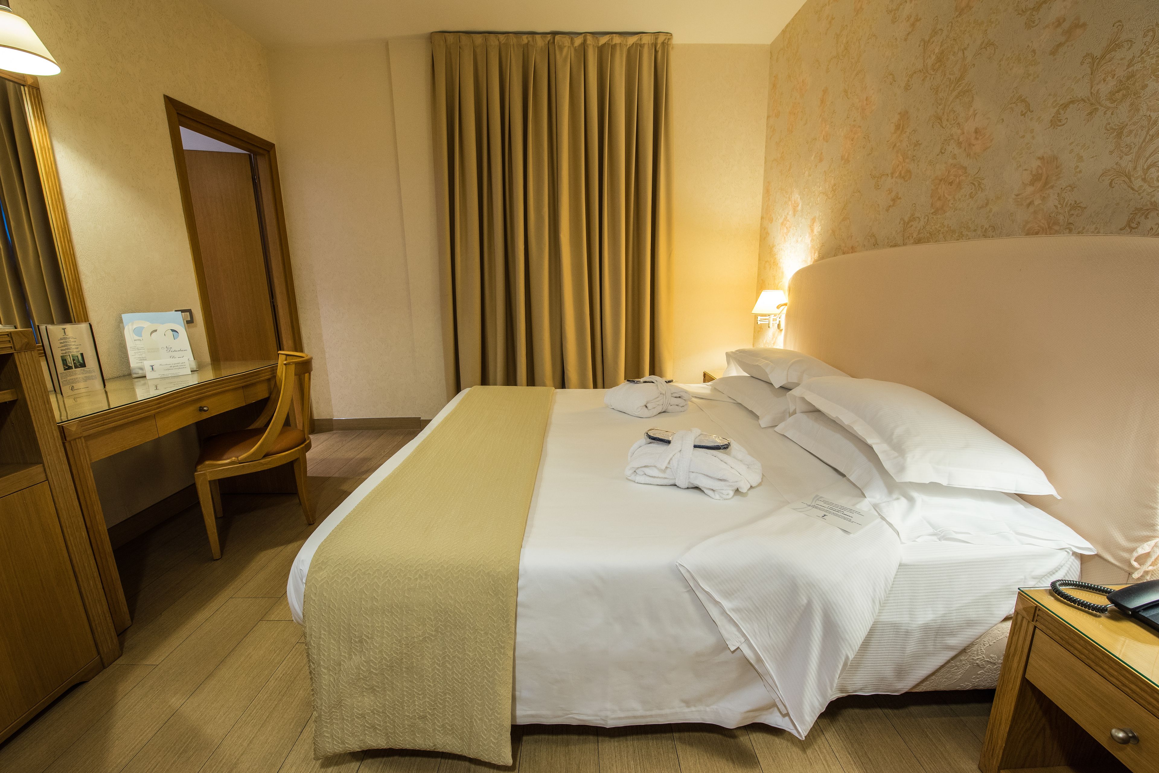 Une chambre d’hôtel avec un lit, un bureau, une chaise, une lampe et une table de chevet.