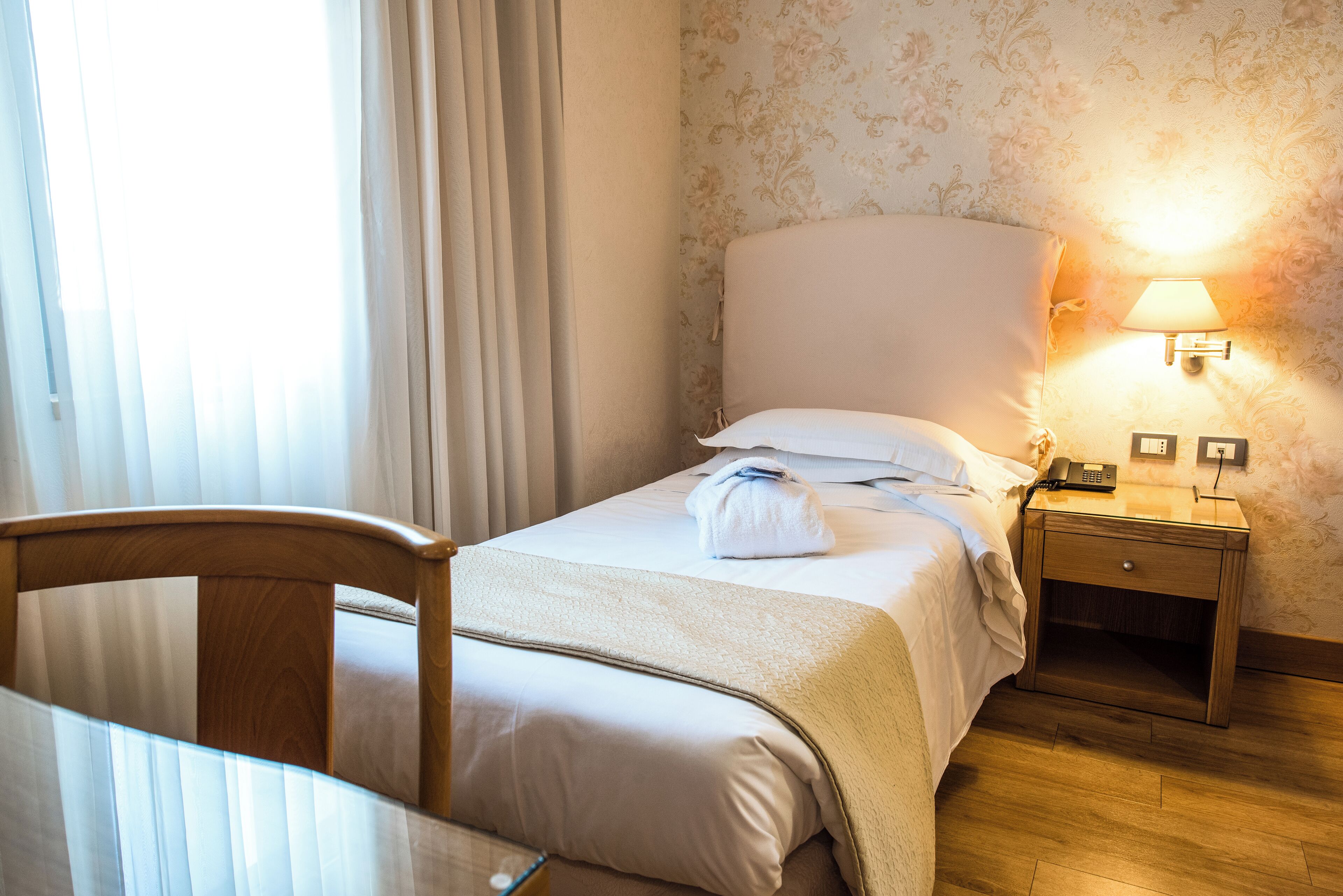 A hotel room with a bed, a bedside table with a lamp, and a chair.