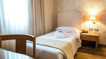 A hotel room with a bed, a bedside table with a lamp, and a chair.