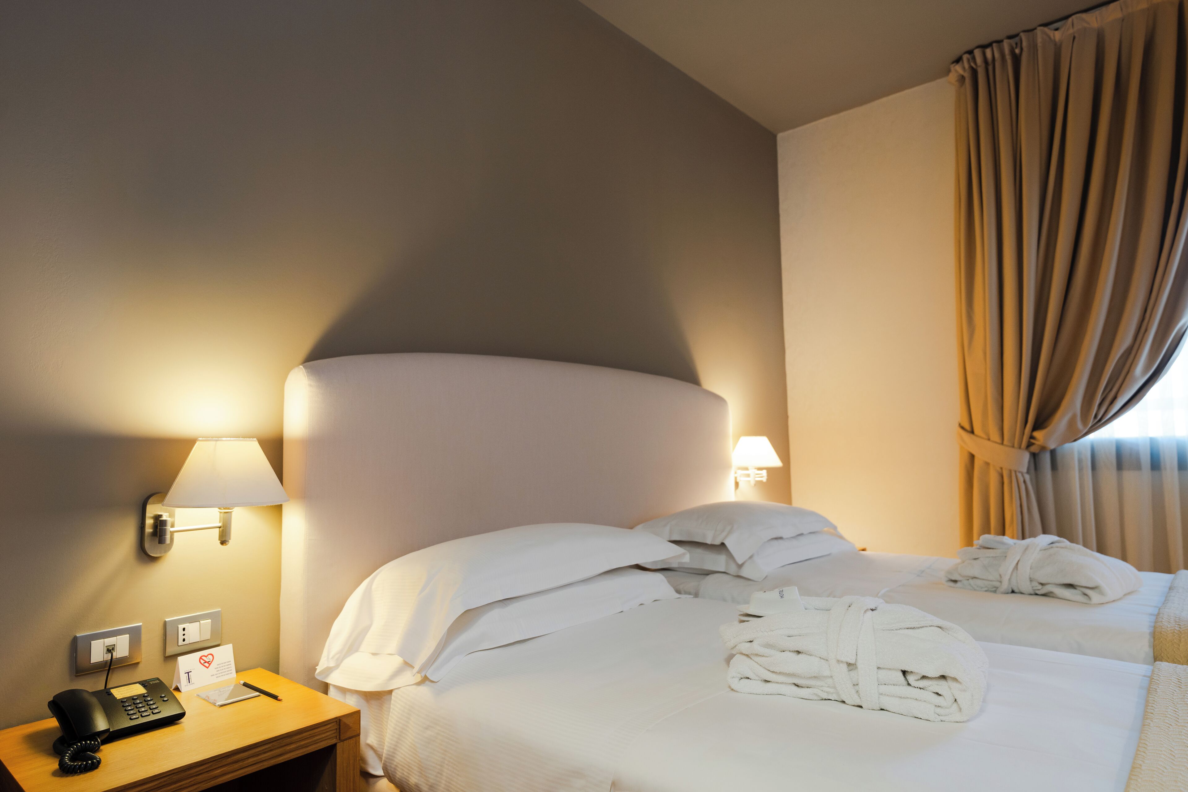 Hotelkamer met een bed, twee bedlampen, telefoon, notitieboekje en een bordje met vermelding van 24-uurs service.