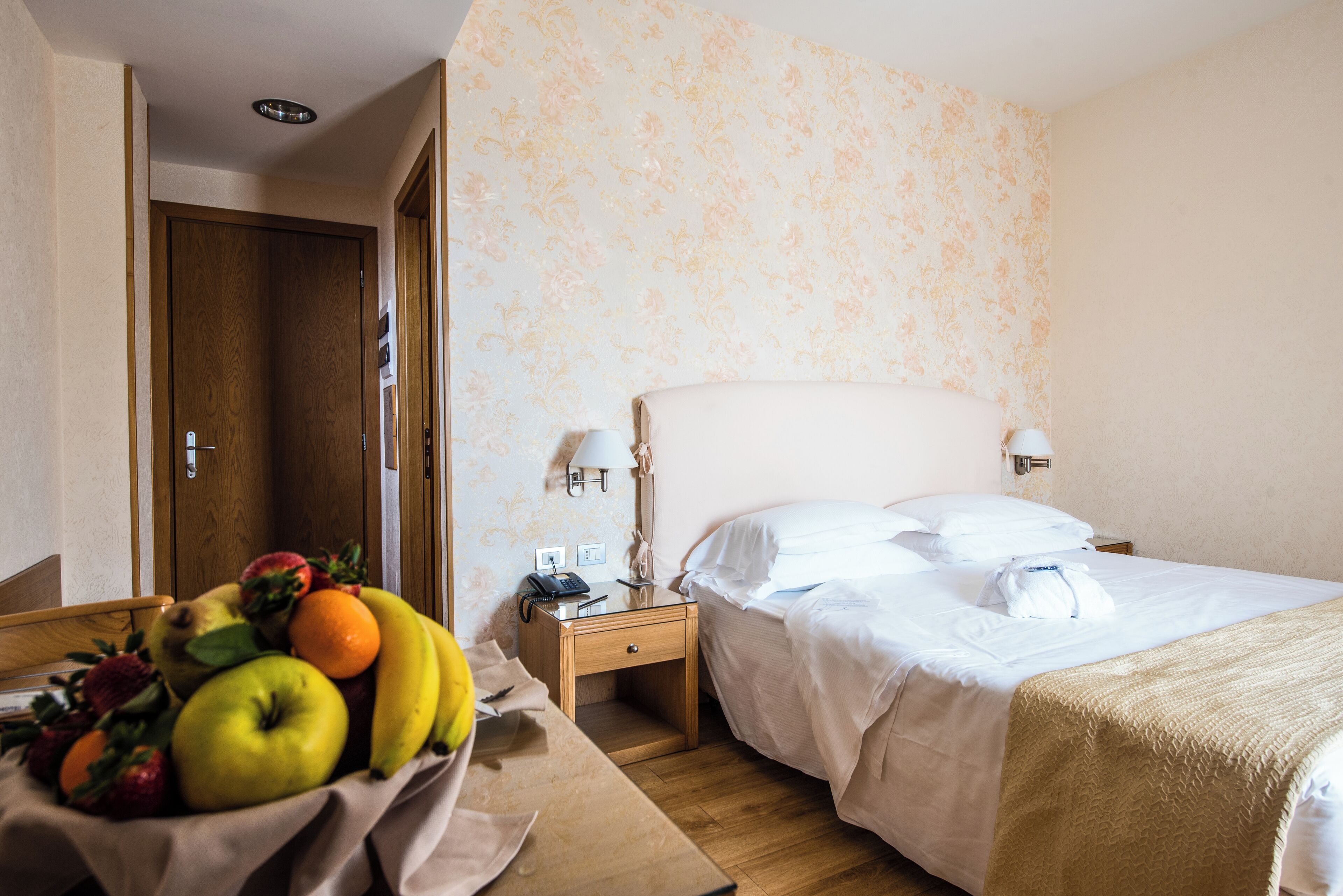 Habitación de hotel con cama, mesita de noche y una cesta de frutas.