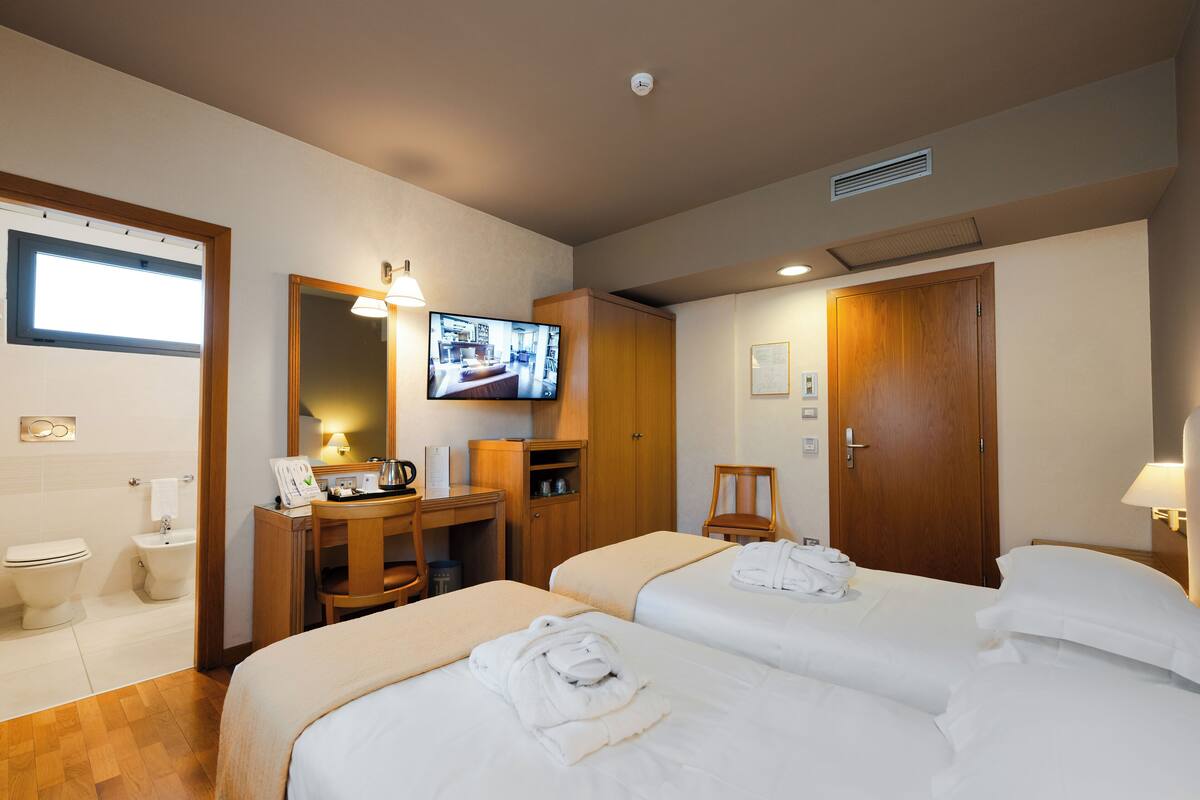 A hotel room with two beds, a desk, a television, and a bathroom.