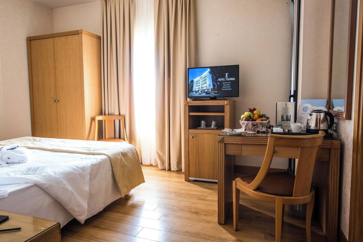 A hotel room with a bed, a desk with a chair, a television, and a wardrobe.