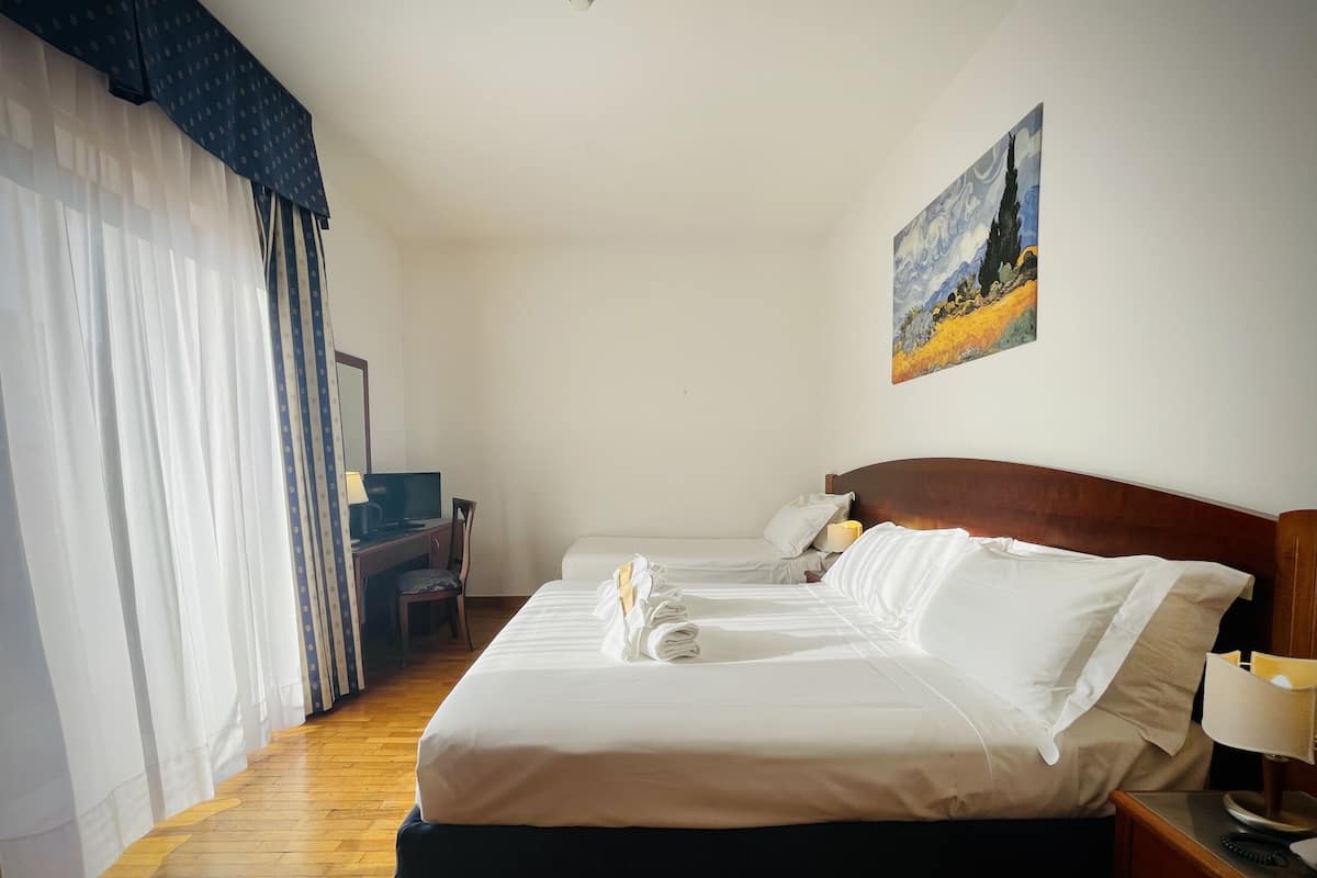 A hotel room with a large bed, a desk with a chair, a television, and a painting on the wall.