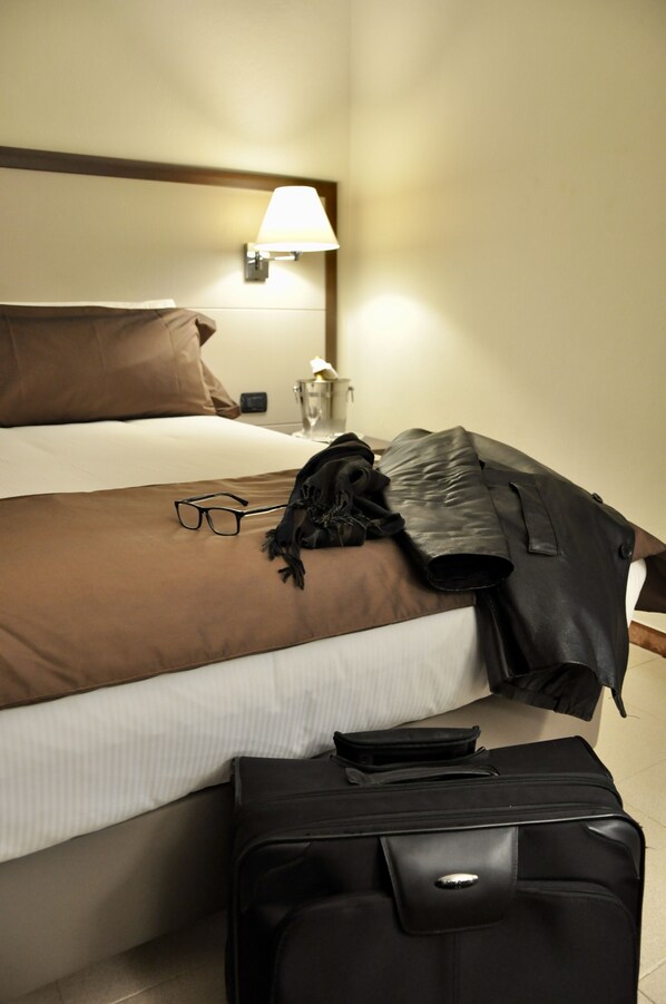 Una habitación de hotel con una cama, una lámpara, una maleta y un par de gafas sobre la cama.