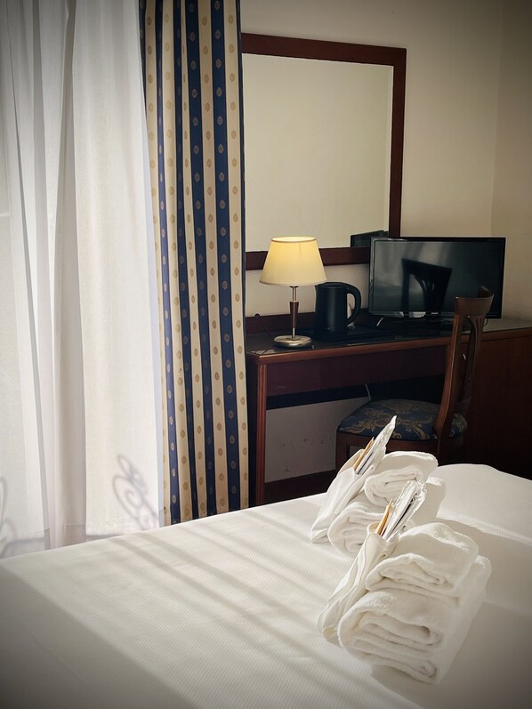 Habitación de hotel con una cama bien tendida, un escritorio con lámpara, un televisor y una silla.