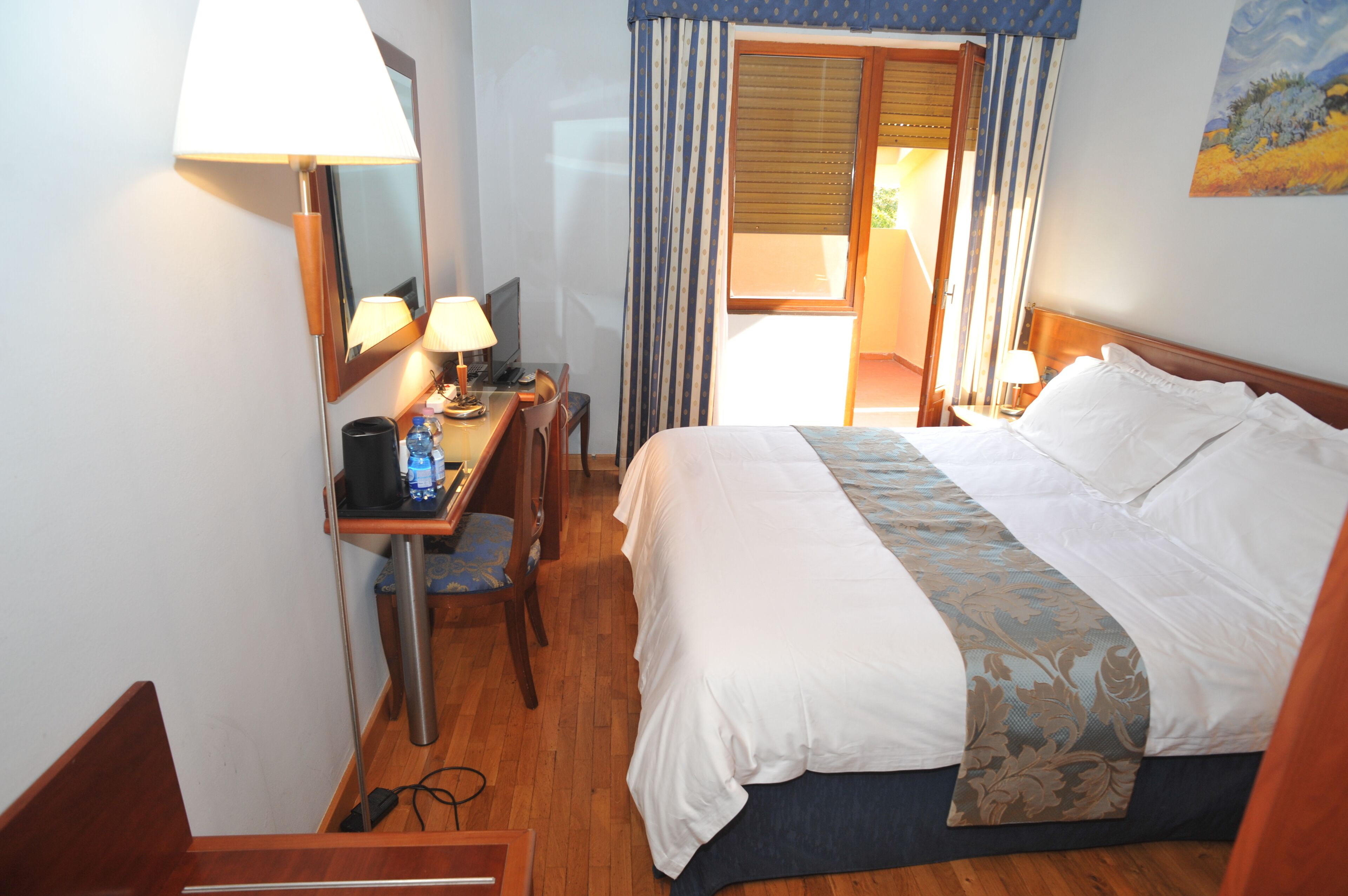 Habitación de hotel con cama, escritorio, silla y ventana con cortinas.