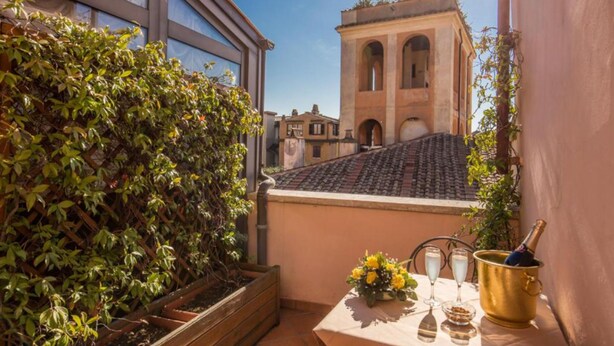 Un balcón con vistas a un edificio histórico, una mesa con una botella de champán y un arreglo floral.