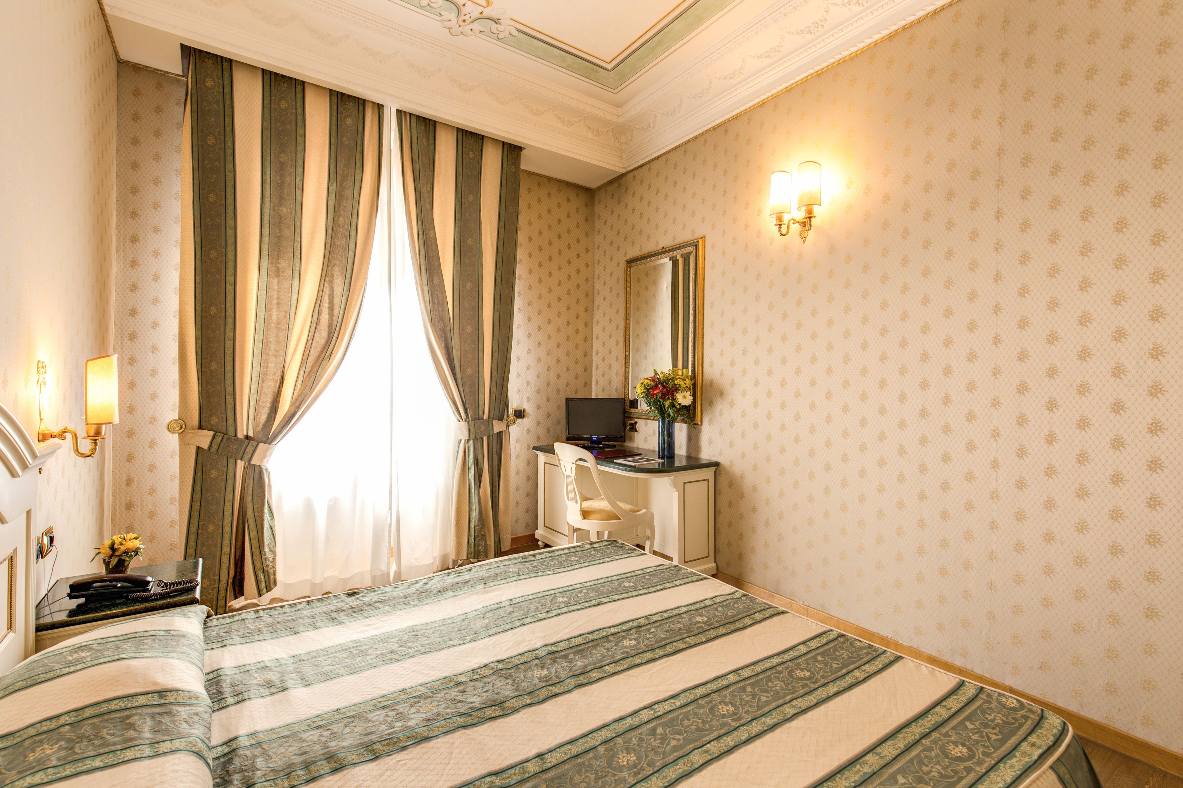 A hotel room with a large bed, a desk with a computer, a chair, and a mirror on the wall.