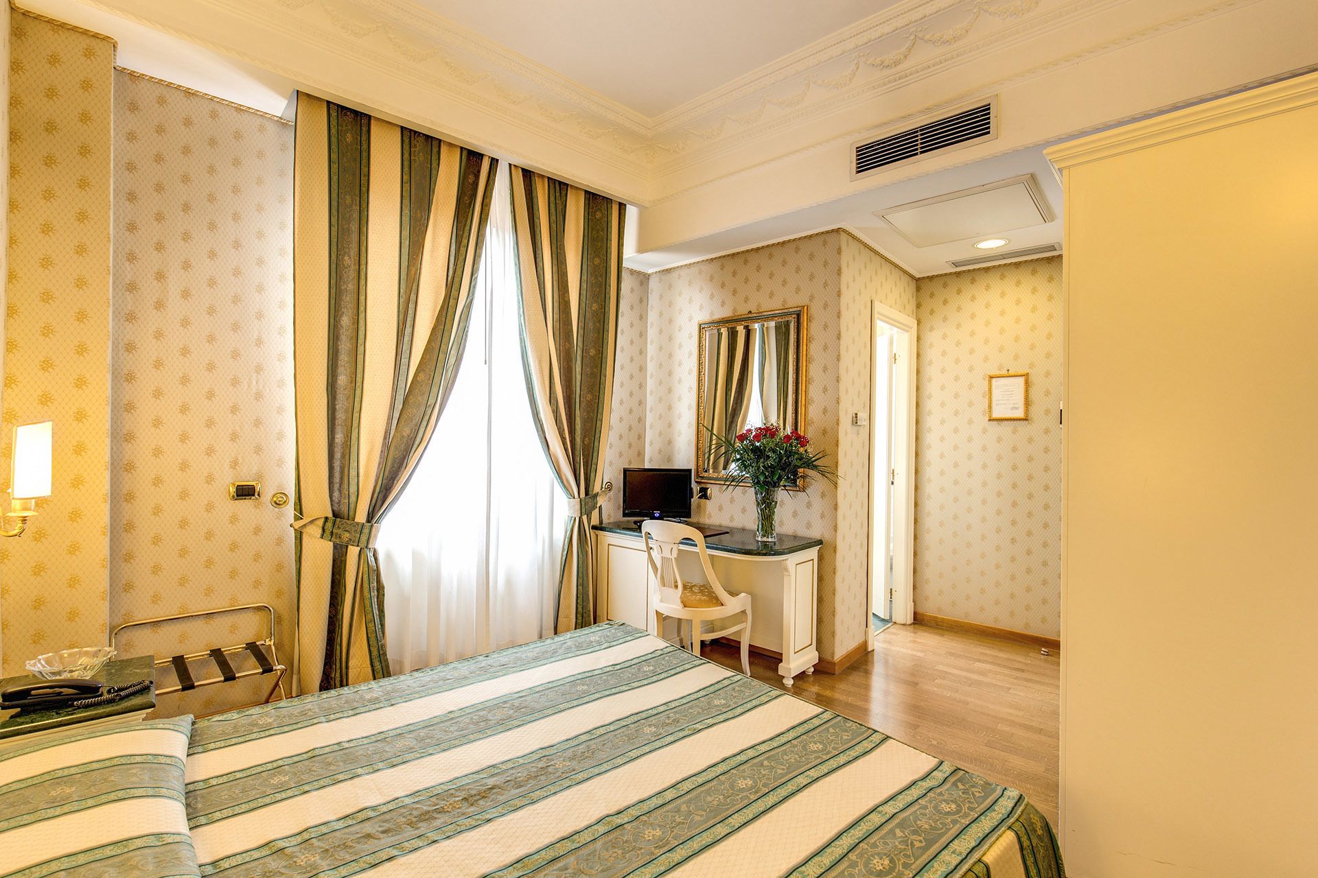 Una habitación de hotel con una cama, un escritorio, una silla, un ordenador y un espejo.