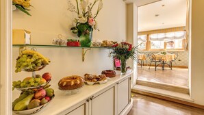 Una mesa de buffet con frutas, bollería y un florero.