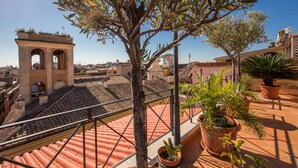 Una terraza en la azotea con tejas de terracota, plantas en macetas y vistas de la ciudad.