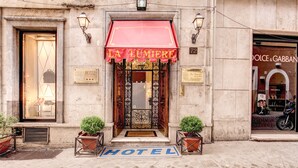 Entrada de hotel con toldo rojo, un letrero que dice "HOTEL" y una calle adoquinada.