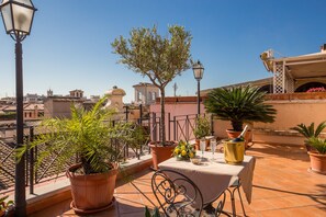 A rooftop terrace with potted plants, a table with a tablecloth, and a clear view of the cityscape in the background. - Hotel La Lumiere di Piazza di Spagna (Rome)