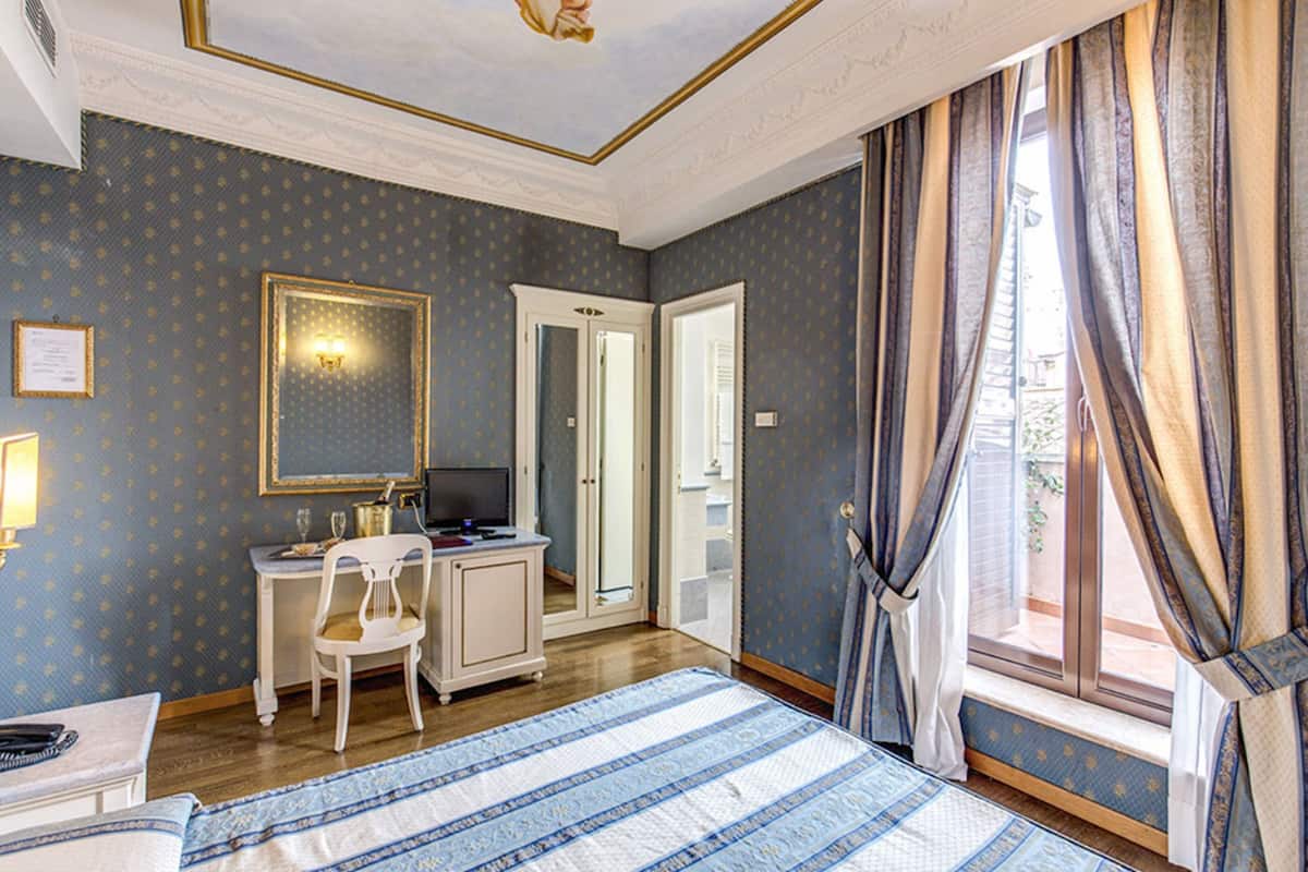 Une chambre d’hôtel avec un lit, un bureau et une chaise, un miroir et une fenêtre avec des rideaux.