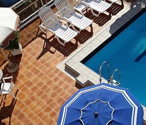 Zona de piscina amb gandules blanques i un parasol blau.