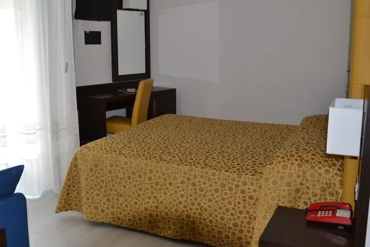 A hotel room with a bed, a desk, a chair, a telephone, and a window with curtains.