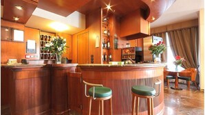 Uma área de bar com balcões de madeira, banquetas estofadas verdes e um aparador de vinhos.