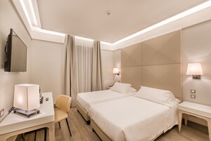 Habitación de hotel con dos camas, un escritorio con lámpara, una silla y un televisor.