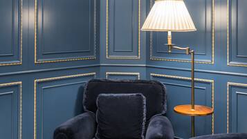 Ein Zimmer mit dunkelblauen Paneelwänden, einem schwarzen Sessel mit Felldecke und einem kleinen Holztisch.