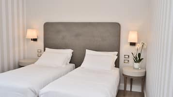 Une chambre d’hôtel avec deux lits simples, une tête de lit grise, des lampes de chevet et une petite table avec une plante.