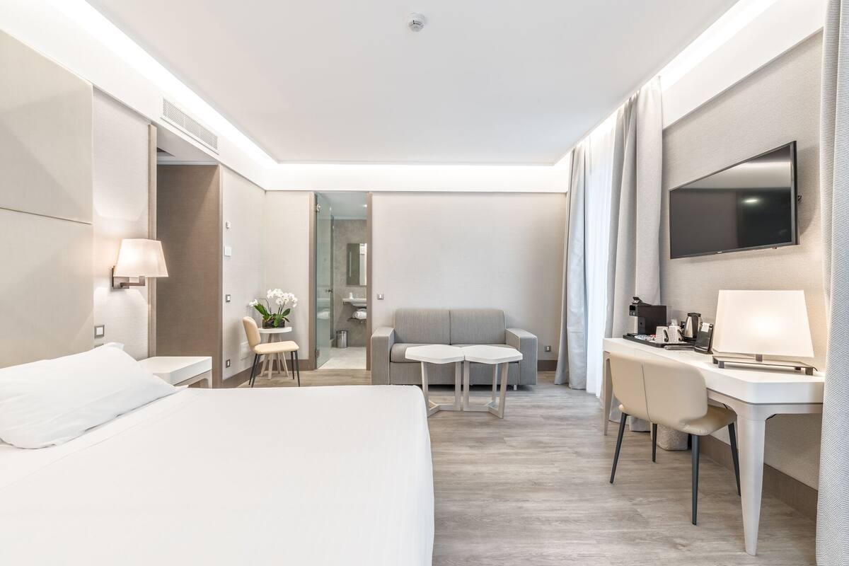 Een moderne hotelkamer met een groot bed, een bureau met stoel, een bank en een aan de muur bevestigde televisie.