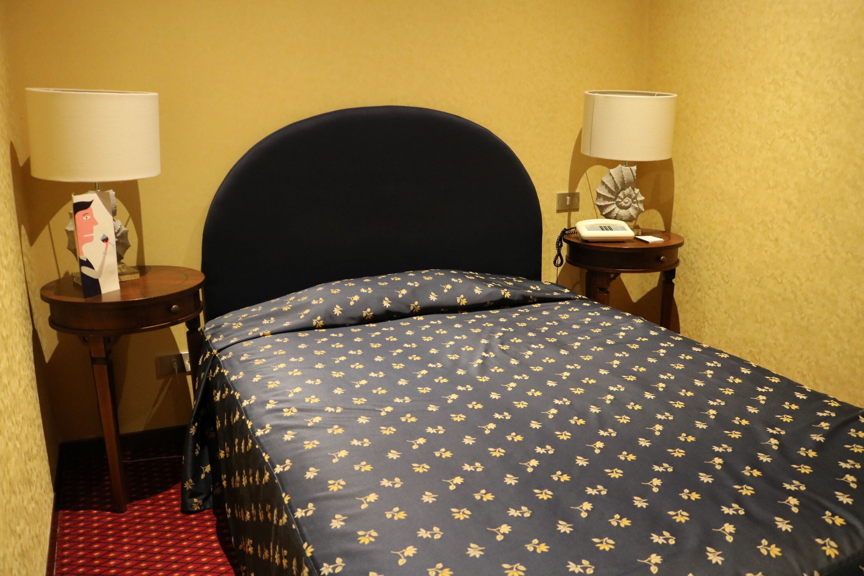 A hotel room with a bed, two bedside tables, a lamp, a telephone, and a decorative item on one of the tables.