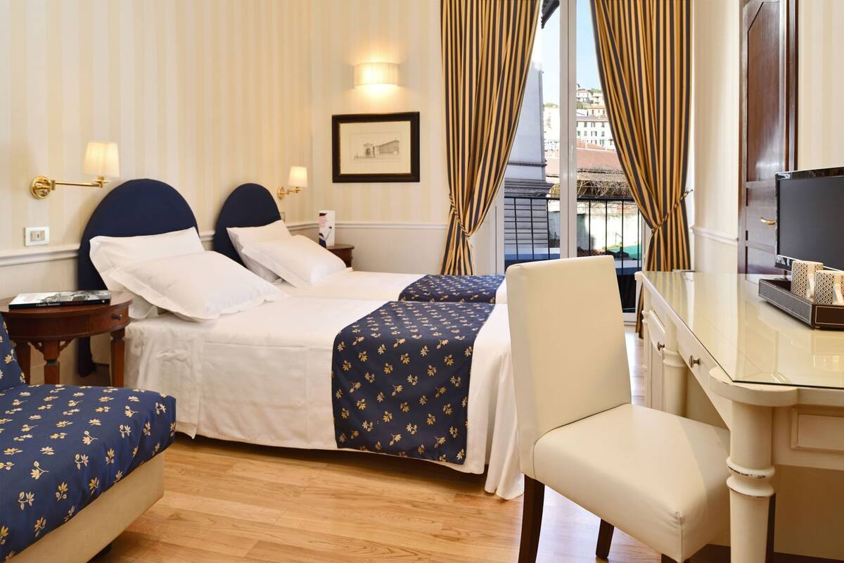 Een hotelkamer met een bed, twee nachtkastjes, een stoel, een bureau en een raam met gordijnen.