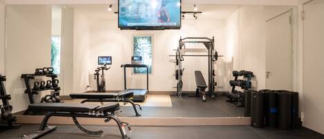 Un gimnasio moderno con equipo de ejercicio, una pantalla de televisión y un espejo grande.