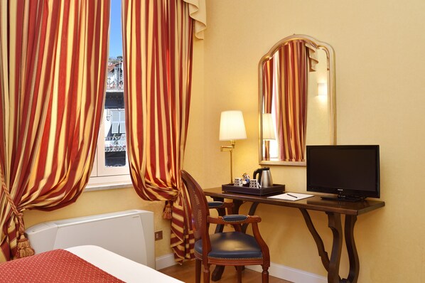 Habitación de hotel con cama, escritorio, computadora, silla, lámpara y un espejo grande.