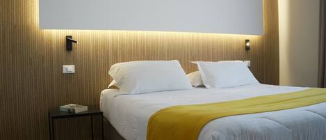 A modern hotel room with a bed, bedside tables, and a wall-mounted light fixture.