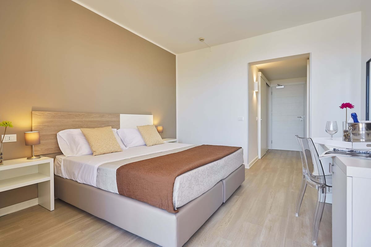 Una habitación de hotel moderna con cama, mesita de noche, lámpara y un escritorio con silla.