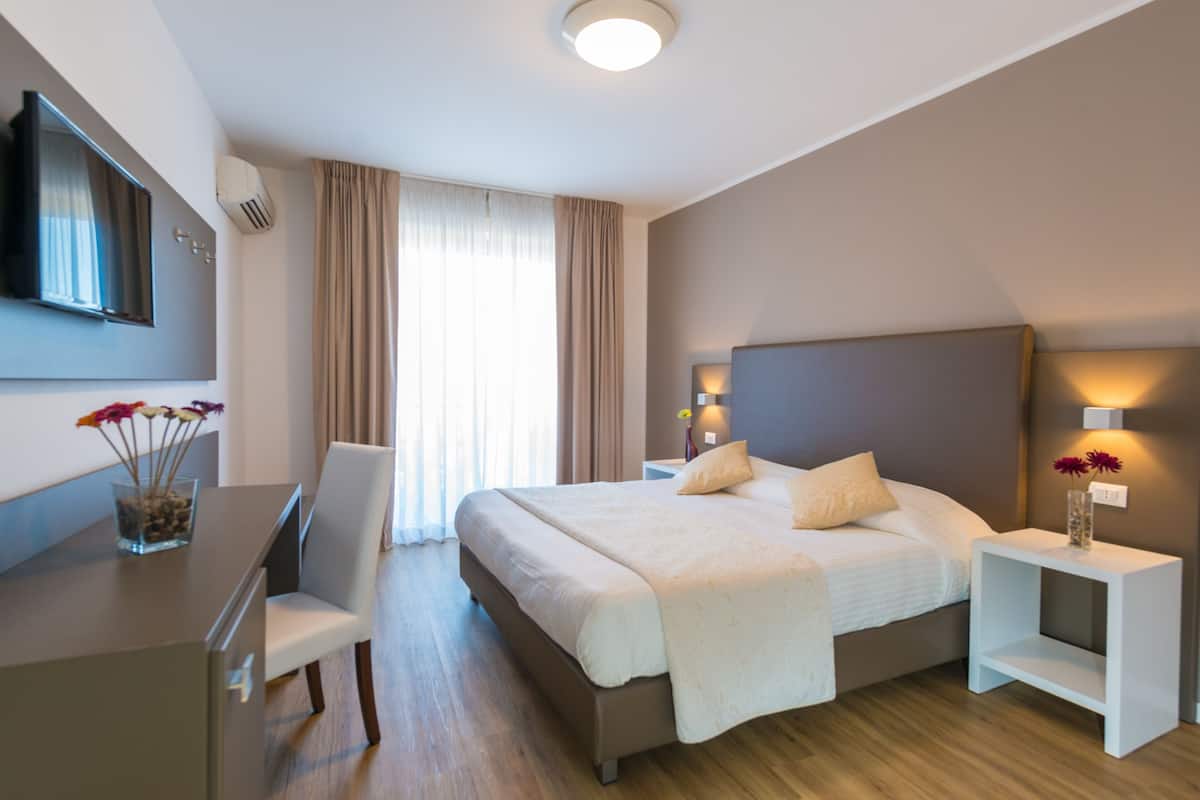 Una habitación de hotel moderna con una cama grande, un escritorio y un televisor montado en la pared.