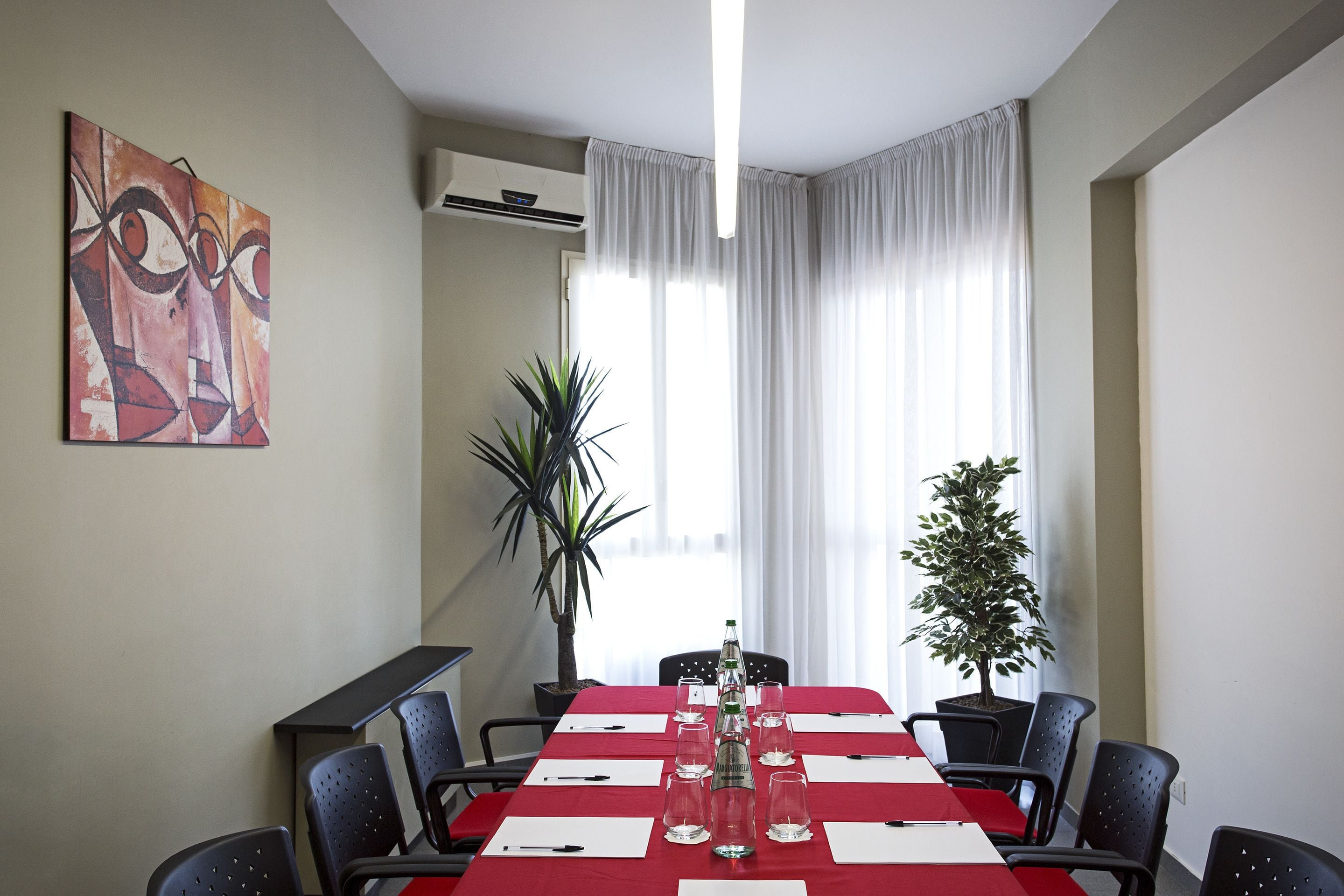 Una sala conferenze con un tavolo rosso, sedie nere, una pianta in vaso e un quadro appeso al muro.