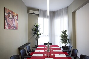 Una sala conferenze con un tavolo rosso, sedie nere, una pianta in vaso e un quadro appeso al muro.