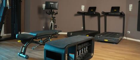 Een sportschool met trainingsapparatuur, waaronder een bank, loopband en hometrainer.