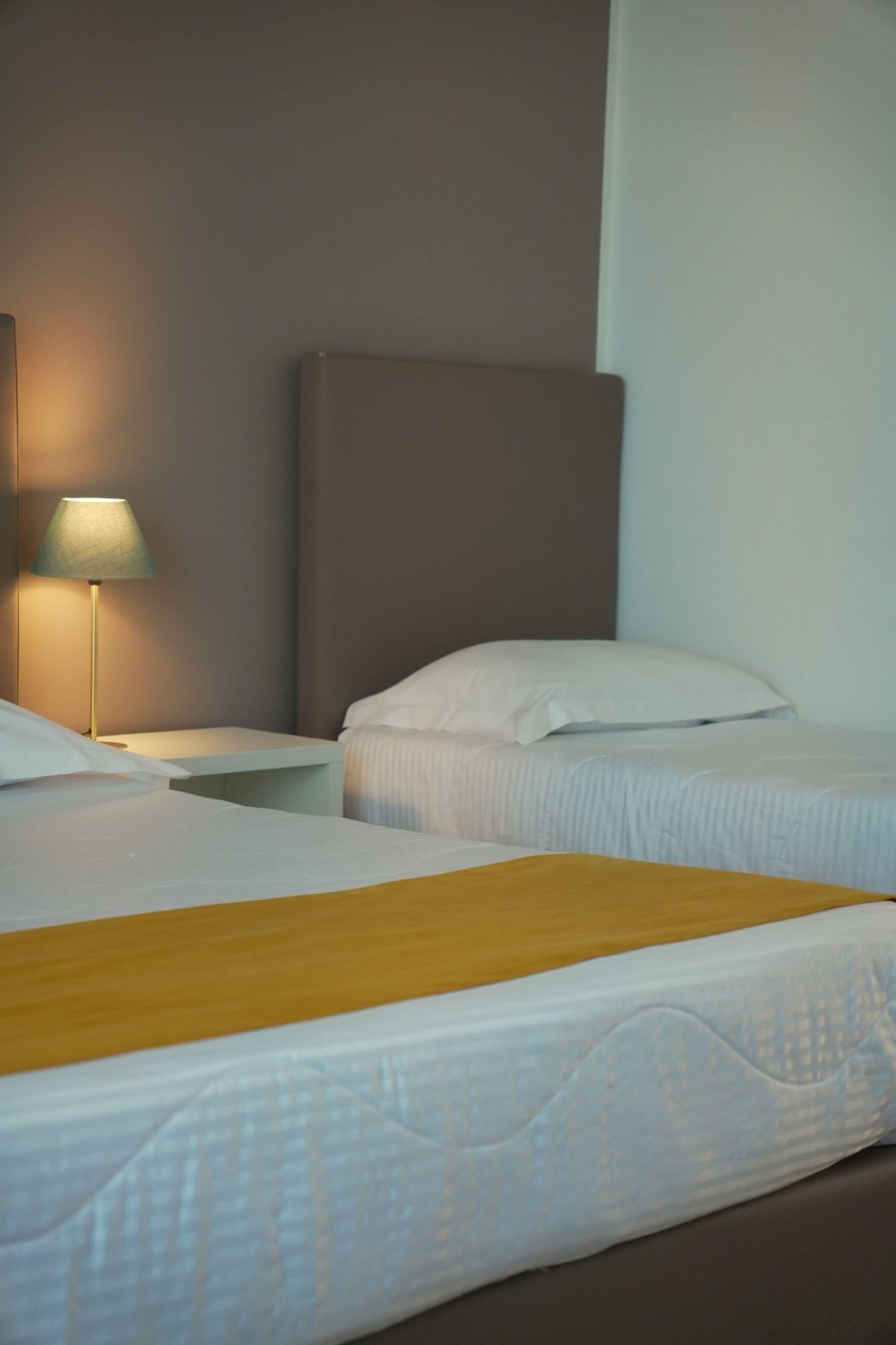 Ein Hotelzimmer mit zwei Betten, einem Nachttisch mit Lampe und einem Kopfteil.