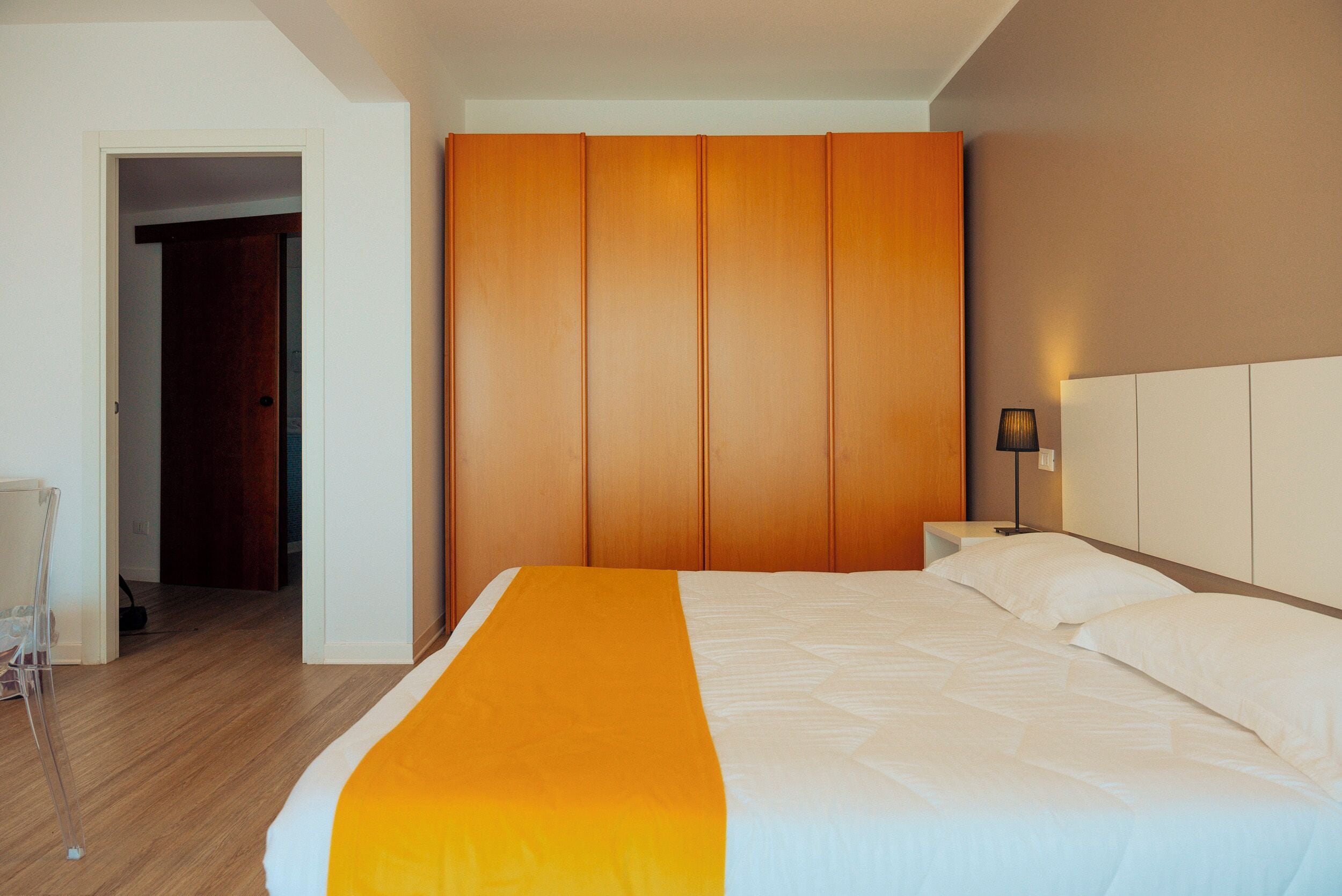 A hotel room with a bed, a wooden wardrobe, a nightstand, and a lamp.