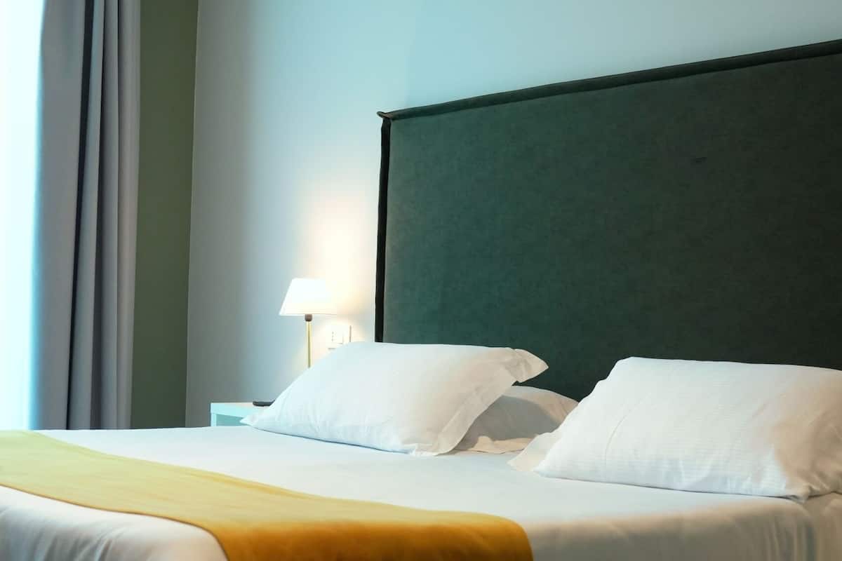 Habitación de hotel con cama, mesita de noche, lámpara y ventana con cortinas.